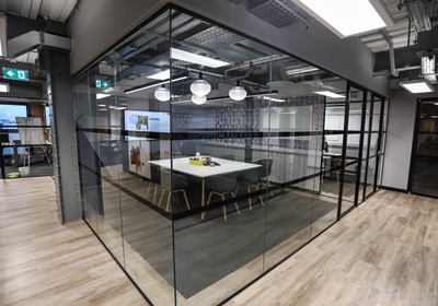 A modern office featuring a glass partition, with a table and chairs arranged for meetings.
