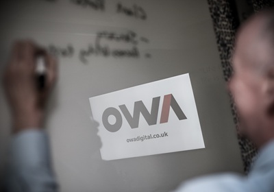 OWA Digital staff collaborating on a whiteboard in the background.