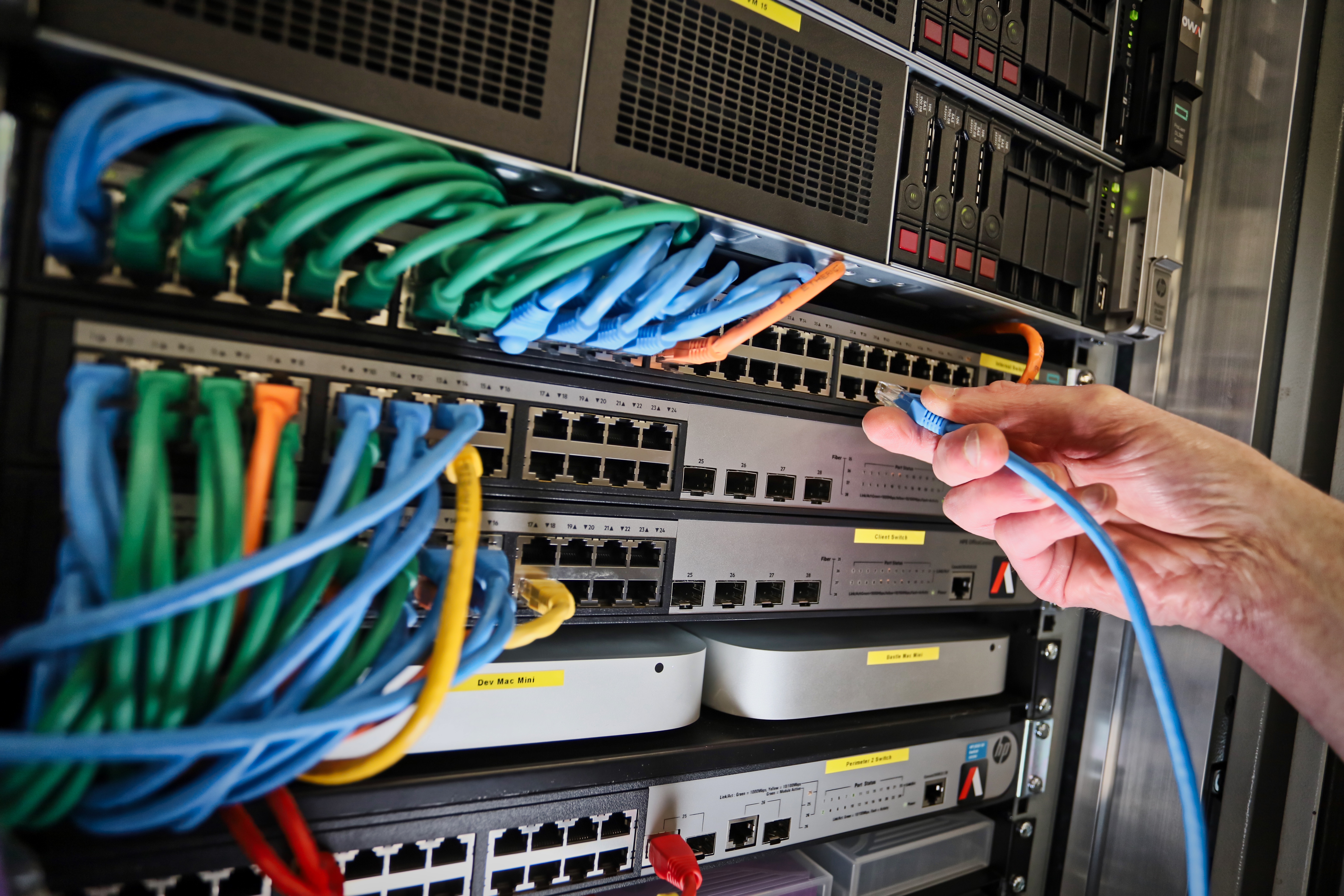A person holds a cable while connecting it to a server in a data center environment.