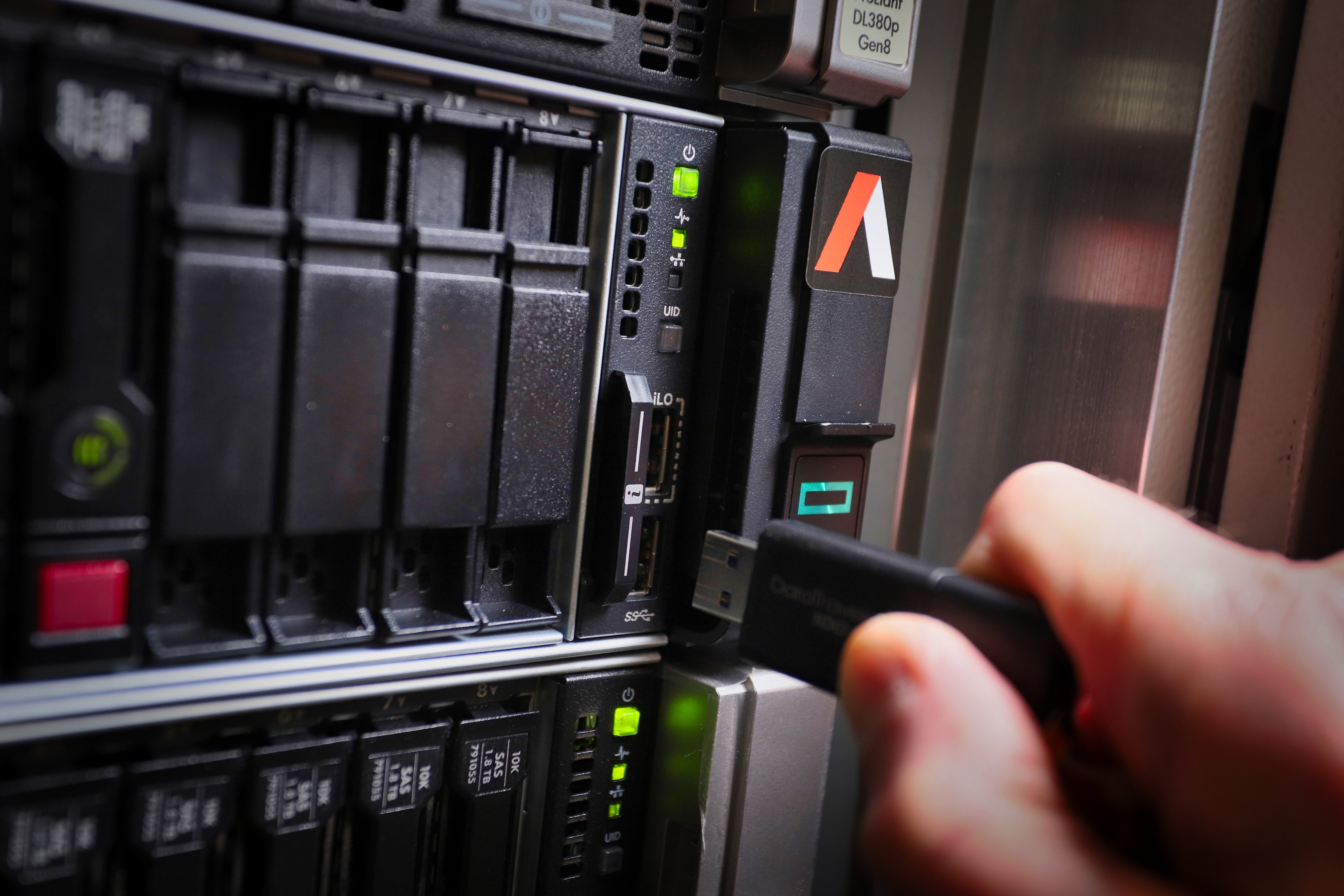 A person holds a USB stick in front of a server, indicating a data transfer or connection process.