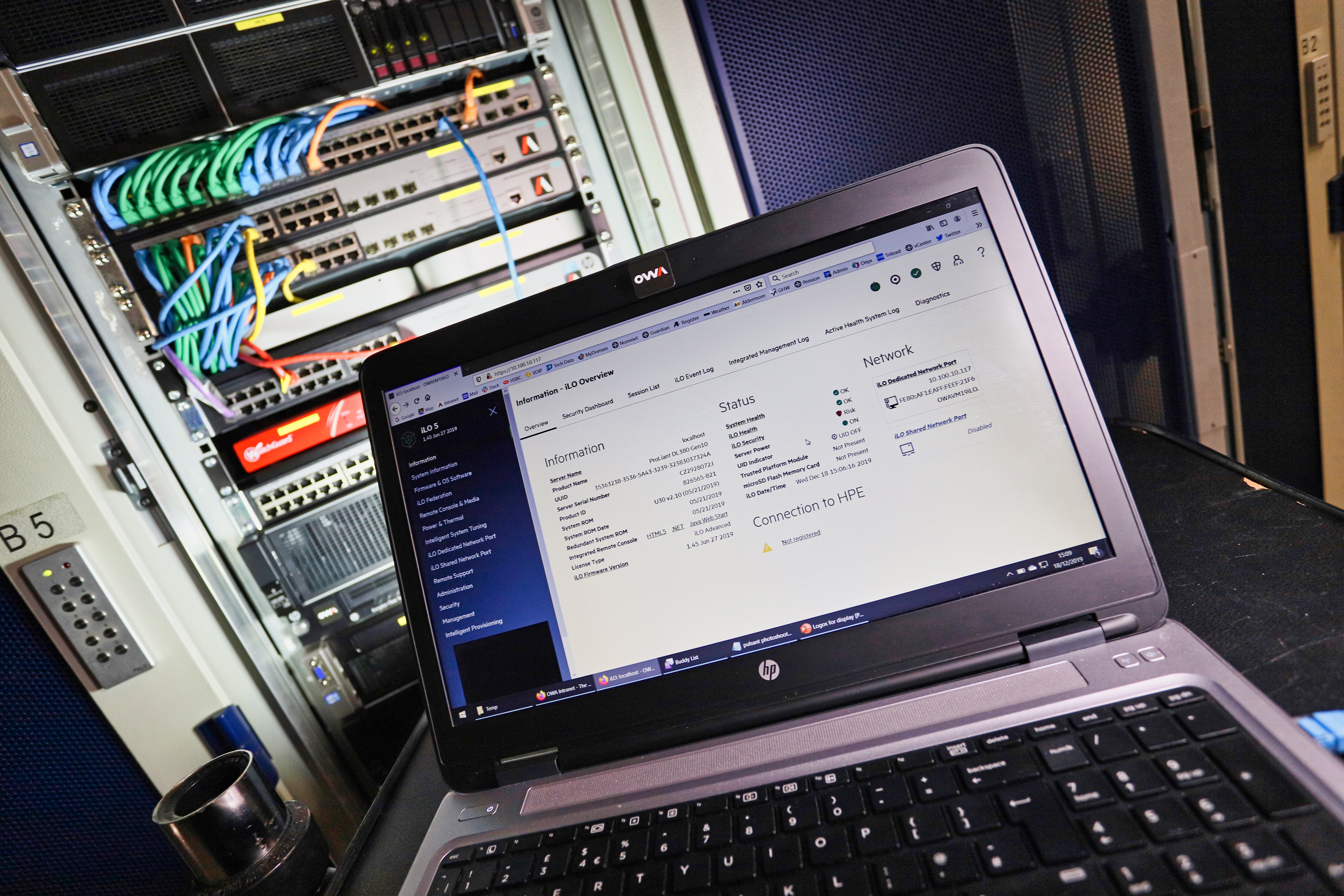 A laptop computer placed on a desk, in front of a rack of servers.