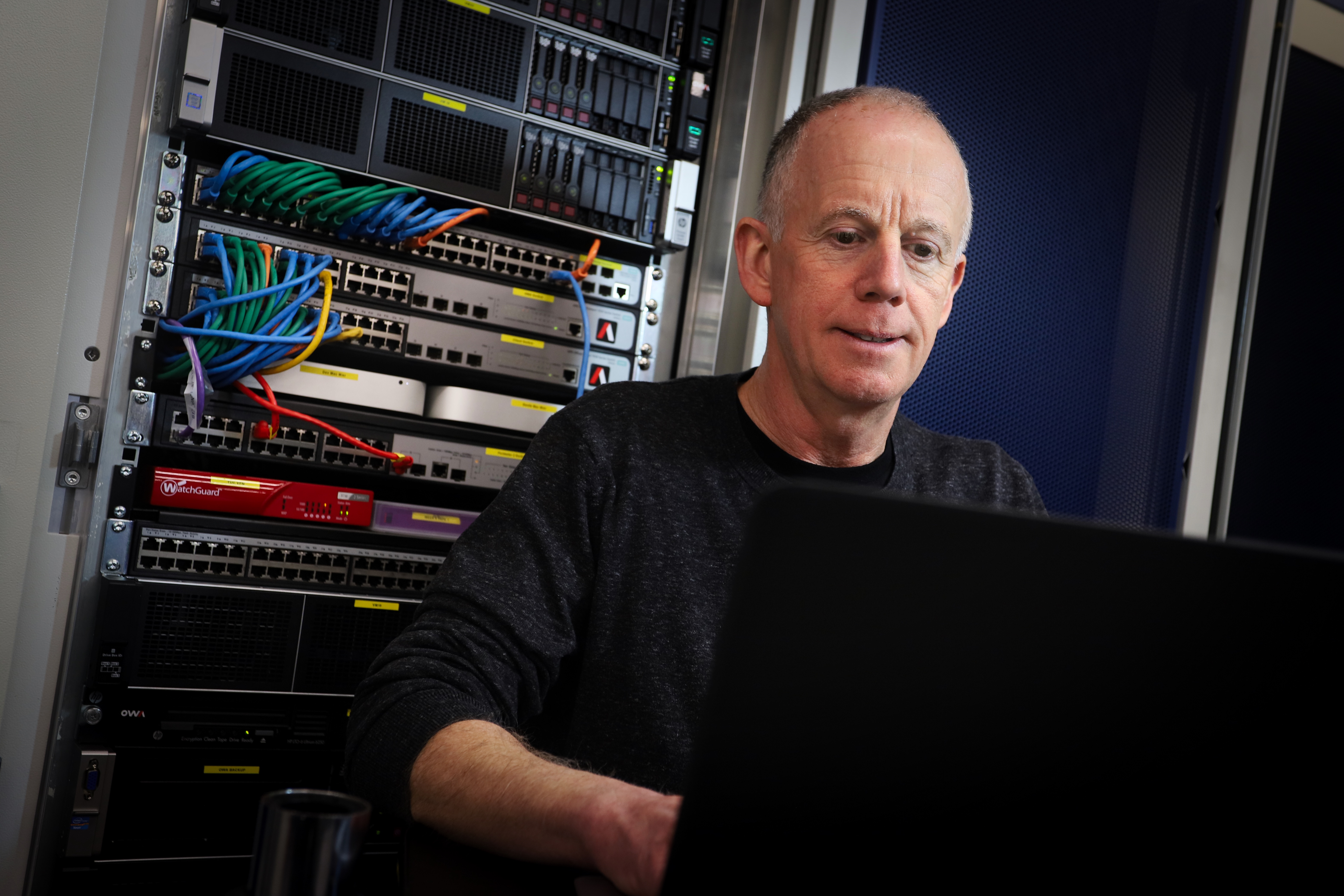 A man engaged in work, seated in front of a computer, with a thoughtful look on his face.