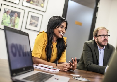 Two people engaged in a client meeting at OWA Digital, sitting at a table with laptops open in front of them.